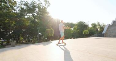 bonito jovem macho com skate ao ar livre na cidade ouvir música com fones de ouvido video