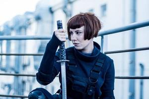 portrait of young redhead woman with japanese sword dressed in futuristic cyberpunk costume standing on the roof. photo