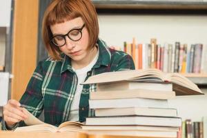 joven pelirroja con gafas lee un libro en la biblioteca foto