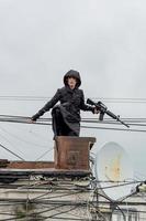 Young woman in modern black techwear style with rifle posing on the rooftop, portrait of redhead woman cyperpunk or post apocalyptic concept photo