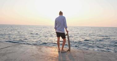 jeune beau mâle ride sur la planche à roulettes, mer et coucher de soleil sur fond video