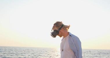 retrato de jovem macho bonito na praia usando óculos de realidade virtual, lindo nascer do sol no fundo video