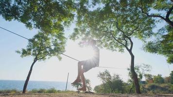 Athlete walking in slackline in the park with sea and blue sky on background video