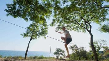 athlet, der in der slackline im park mit meer und blauem himmel im hintergrund spaziert video