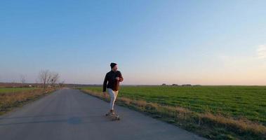 paseo masculino joven en patineta longboard en la carretera del país en un día soleado video
