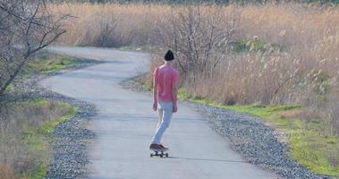 jovem passeio masculino no skate longboard na estrada rural em dia ensolarado