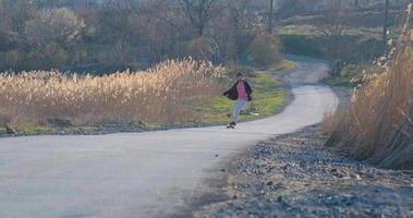 giovane maschio giro su skateboard longboard sulla strada di campagna in una giornata di sole video