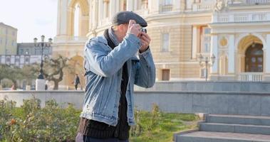 junger gutaussehender männlicher reisender mit filmkamera macht straßenfotos video