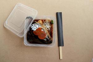 Boiled salmon head with soy sauce, Salmon kabutoni in square plastic box for take home and brown wood background. photo