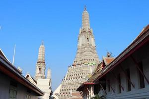 White pagoda in Wat Arun temple and blue sky. Ancient statues around base of pagoda. Wat Arun is a ancient monument in Thailand. photo