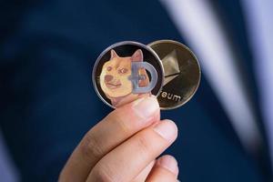 Golden Ethereum ETH Dogecoin DOGE group included with Cryptocurrency on hand business man wearing a blue suit. Filed and put and give to me. Close up and Macro photography concept. photo