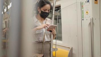 hermosa dama asiática usa máscara para sostenerse en el poste dentro del vagón del metro con la cabeza hacia abajo usando el teléfono celular, viajero en el viaje, covid-19 nueva normalidad, riesgo en el transporte público, distancia social, usuario de teléfono inteligente video