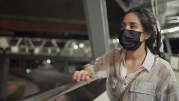 menina bonita asiática usa máscara protetora preta descansando o braço na travessia da borda da ponte pensando aliviar, risco de cautela sair, pedestre andando no fundo, distanciamento social novo normal, noite