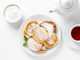 Cheesecake, curd fritters. Cottage cheese pancakes with powdered sugar. Sweet fried cheese pancakes on white plate on white background. Top view. Home tea party photo