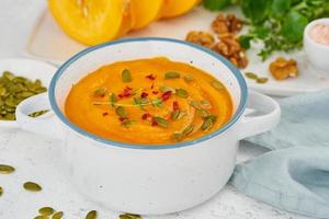 Pumpkin vegetarian cream soup with walnuts, side view on light background closeup photo