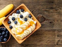 Brown wooden Bowl of homemade curd with banana, jam, blueberries on dark brown wooden background, photo