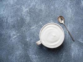 Greek yogurt with jam in white bowl on grey blue concrete stone table, top view, copy space photo