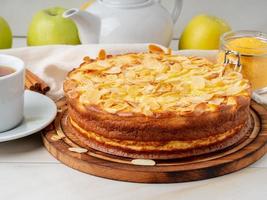 Cheesecake, apple pie, curd dessert with polenta, apples, almond flakes and cinnamon on white marble kitchen table, side view photo