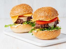 dos hamburguesas en una pizarra blanca de fondo blanco, comida gorda casera caliente e insalubre foto