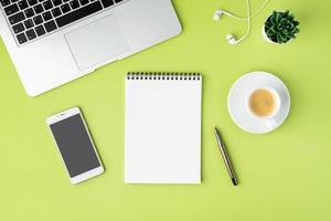 concepto de espacio de trabajo moderno. cuaderno, teléfono inteligente, taza de café, computadora portátil y auriculares sobre fondo verde