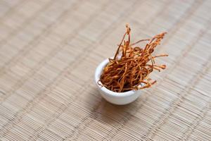 Dry cordyceps militaris mycelium in white bowl with wooden background. Orange medical mushroom for good health. photo