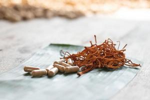 Dry cordyceps militaris on a green banana leaf with wooden background. Orange medical mushroom for good health with capsules. photo