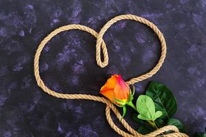 Heart shape made with rope and rose on a dark background. Top view photo