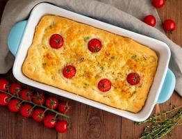 appetizing golden focaccia with tomatoes and spices, on dark wooden rustic table photo