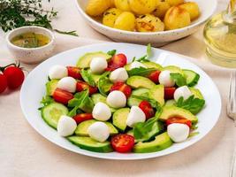 Fresh salad with tomatoes cucumbers arugula mozzarella and avocado. Oil with spices, photo