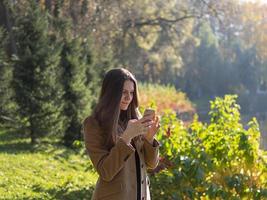 hermosa adolescente en el parque, sosteniendo un teléfono inteligente y chateando en línea en internet. mujer joven con pelo largo