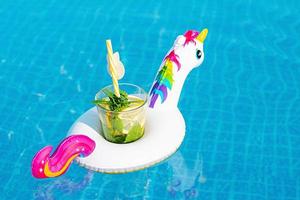 mojito de cóctel fresco en un juguete inflable de unicornio blanco en la piscina. concepto de vacaciones. foto