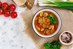 Stew with meat and vegetables in tomato sauce on white background. Top view photo