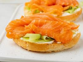 Two open sandwiches with salmon, cream cheese, cucumber slices on white marble table, close up photo