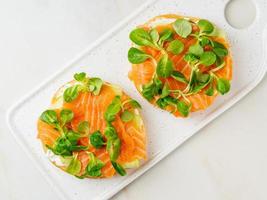 Two open sandwiches with salmon, cream cheese, cucumber slices on white marble table photo