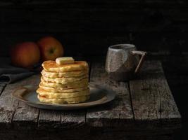 Pancake with butter and cup of tea. Dark moody old rustic wooden background. photo