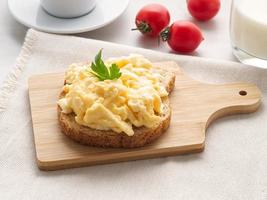 Sandwich with pan-fried scrambled eggs on wooden cutting board, side view. photo