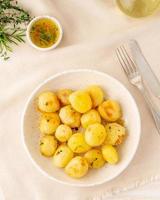 baked in oven with spices round whole potato tubers in plate on white textile background, vertical, top view photo