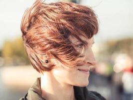 retrato de primer plano de una mujer hermosa con cabello castaño revoloteando en el viento. día soleado de otoño, calle en el centro de la ciudad foto