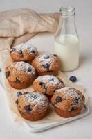 muffin de arándanos, vista lateral, vertical. pastelitos con bayas en mesa de hormigón blanco, desayuno con pastel y leche foto