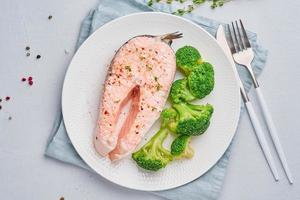 dieta de salmón al vapor, brócoli, paleo, ceto o fodmap. plato blanco sobre mesa azul, vista superior foto
