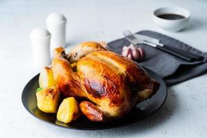 Grilled whole chicken in black plate on white table, baked meat with potatoes. Side view photo