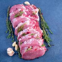 Pork steak, raw carbonate fillet on dark background, meat with rosemary, garlic seasonings, top view