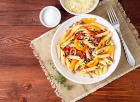 Penne pasta with yellow tomatoes, red and green vegetables, mincemeat on dark wooden background, top view, copy space photo