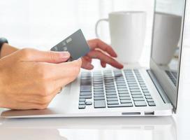 woman sitting at table, drinking tea and looking at laptop, pay for purchases by credit card