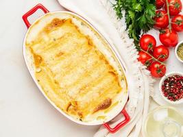 Cannelloni with filling of ricotta and parsley, baked with b chamel sauce, top view, white marble background photo