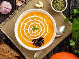 Funny food for Halloween. Pumpkin puree soup, spider web, dark old wooden table, top view. photo