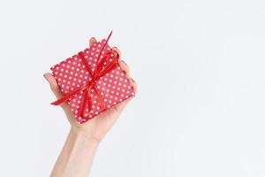 woman hand holding red gift with ribbon, manicured hand with nail polish on white background photo