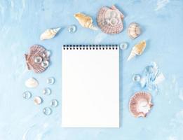 maqueta con marco de concha marina, bloc de notas sobre fondo de piedra azul, espacio de copia. concepto de verano de vacaciones en el mar foto