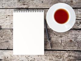open notepad with clean white page, pen and coffee cup on aged old rustic wooden table, top view
