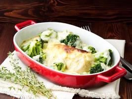 Chicken fillet baked with broccoli in bechamel sauce on dark wooden table. Healthy food photo